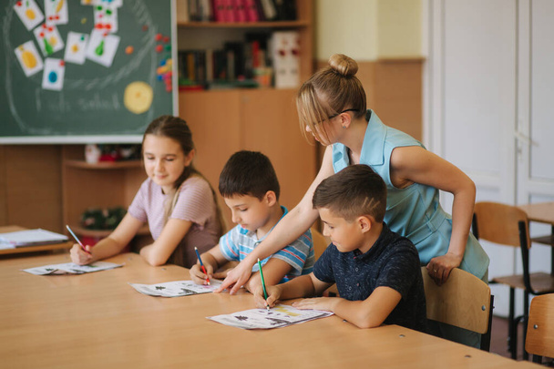 Teacher helping school kids writing test in classroom. education, elementary school, learning and people concept - Photo, Image