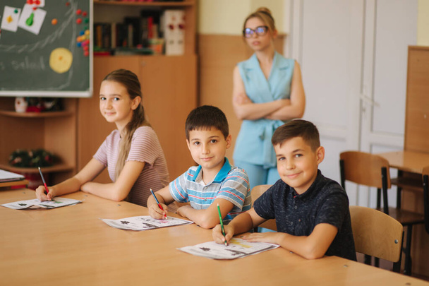 Teacher helping school kids writing test in classroom. education, elementary school, learning and people concept - Photo, Image