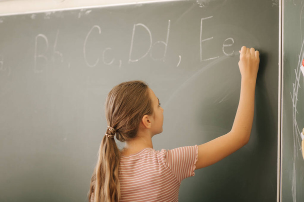 Schoolgirl writing something on blackboard in classroom - Photo, Image
