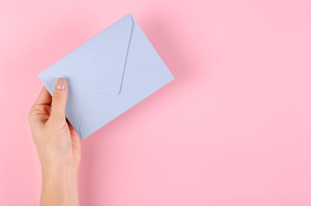 Hand with blue paper envelope composition on pink background. - Fotoğraf, Görsel