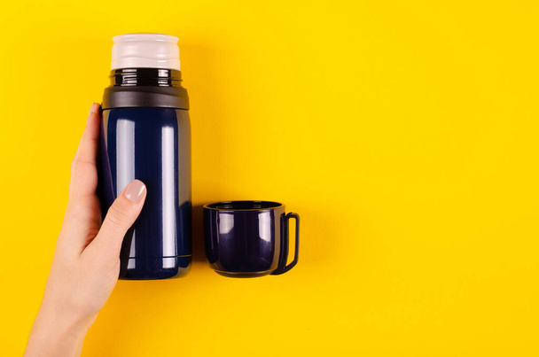 Hand with dark thermos composition on yellow background. - Foto, Imagem