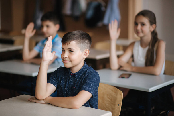 Счастливые маленькие дети в начальной школе. Мальчики и девочки учатся. Дети, поднимите руки
 - Фото, изображение