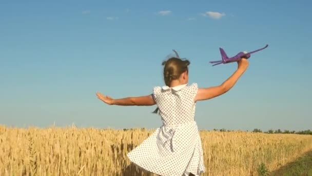 幸せな女の子は日没の光の中でフィールド上のおもちゃの飛行機で実行されます。子供はおもちゃの飛行機で遊ぶ。10代の頃はパイロットになることを夢見ていました。少女はパイロットと宇宙飛行士になりたがっている。スローモーション - 映像、動画