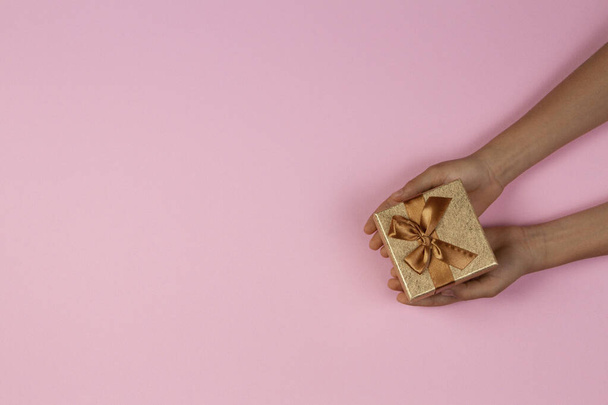 Руки с маленькими подарками коробка на светло-розовом фоне. Вид сверху
 - Фото, изображение