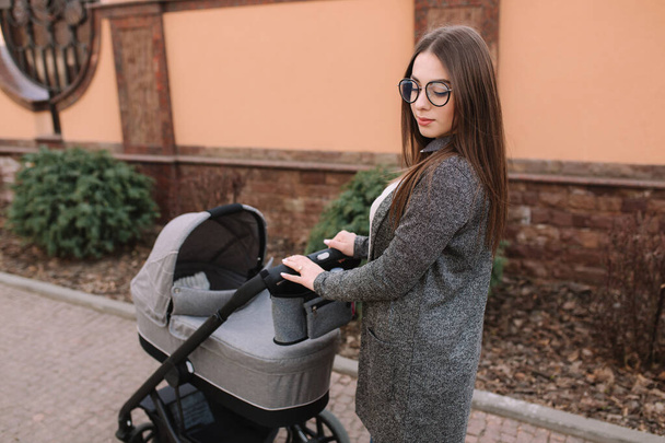 Fiatal anya sétált vele újszülött baba a babakocsi. Szürke Pram. Gyönyörű anya napszemüveg - Fotó, kép