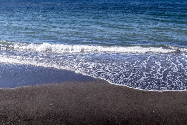 Tengeri szörfözés a tengerparton fekete vulkanikus homokkal. - Fotó, kép