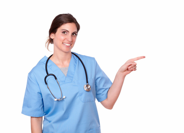 Attractive smiling nurse pointing at her left - Fotó, kép