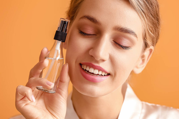 Schöne junge Frau mit kosmetischem Produkt auf farbigem Hintergrund - Foto, Bild