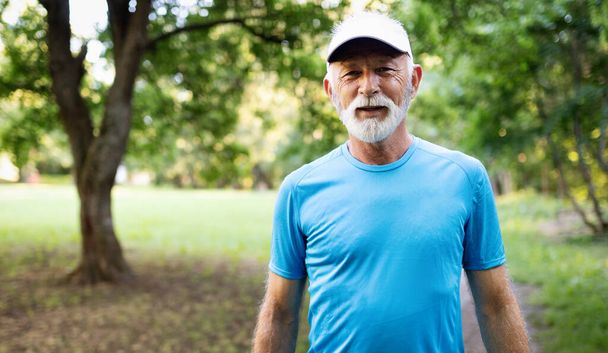 Attractive retired senior man with a nice smile jogging in park - Fotoğraf, Görsel