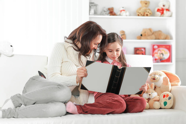 charming mother and daughter reading a book sitting on the couch.photo with copy space - Foto, Imagen