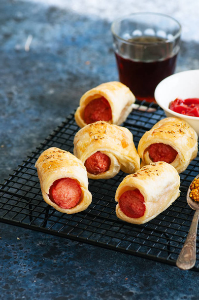 Pigs in a planket - puff pastry rolls with sausages on a wire rack. - Фото, изображение