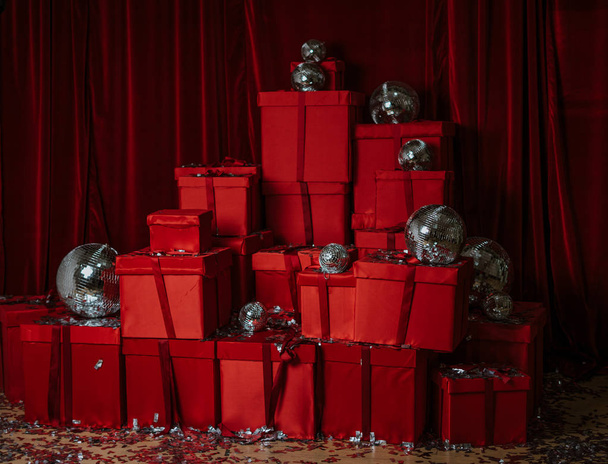 rote Geschenke und Geschenke auf rotem Hintergrund. farbenfrohe Dekoration zum Feiern. Neujahrsparty. Silberne Discokugeln auf rotem Hintergrund - Foto, Bild