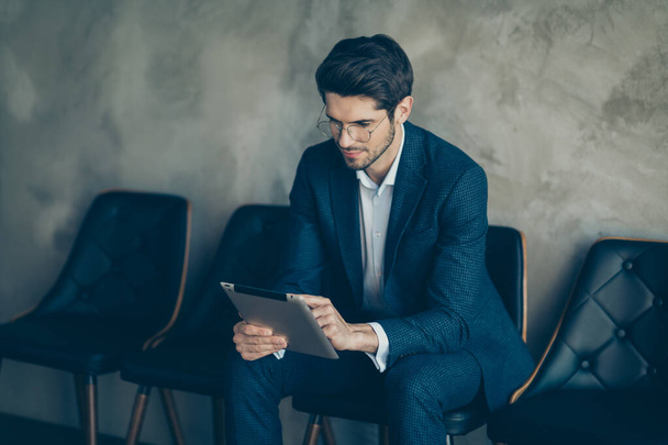 Portrait of focused agent business representative work on his tablet sit on chair wait for meeting with his clients partners wear blue stylish jacket pants isolated over grey color background - Φωτογραφία, εικόνα