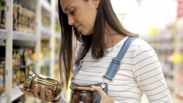 Young woman is chooses canned mushrooms in glass jar at supermarket. - Video