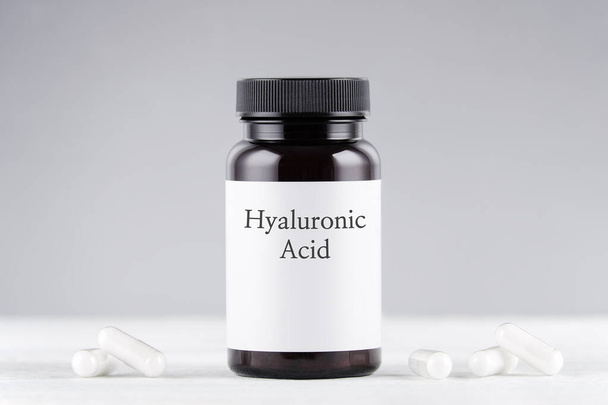 nutritional supplement hyaluronic acid bottle and capsules on gray - Foto, afbeelding