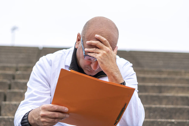 Πρόβλημα στη δουλειά. Απελπισμένος, φοβισμένος, απογοητευμένος ιατρός facepalming ανάγνωση κακά νέα για τα χαρτιά - Φωτογραφία, εικόνα