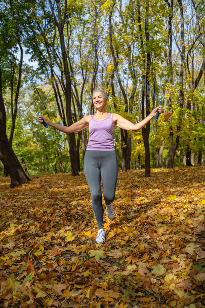 Laughing sportive woman jumping rope on the autumn leaves - Foto, imagen