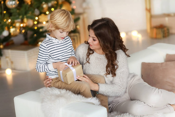 Мама дарит ребенку новогодний подарок и обнимает его
 - Фото, изображение