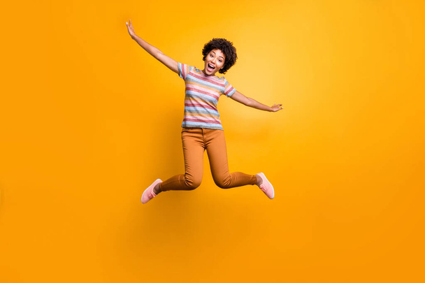 Full length body size photo of cheerful pretty girlish youngster with hands like spreading wings orange trousers striped t-shirt curly wavy isolated vivid color background - Foto, Imagem