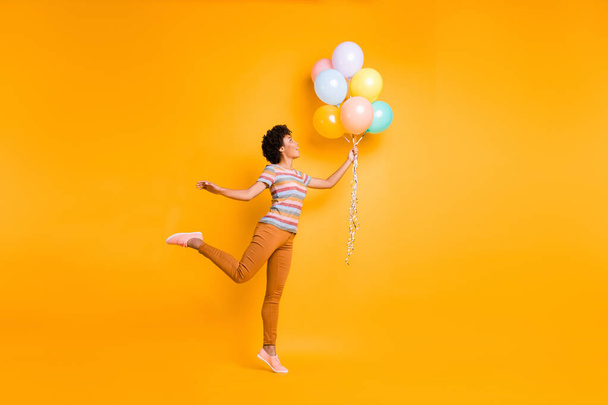 Full length body size view of nice attractive cheerful cheery wavy-haired girl holding in hand air balls having fun isolated over bright vivid shine vibrant yellow color background - 写真・画像