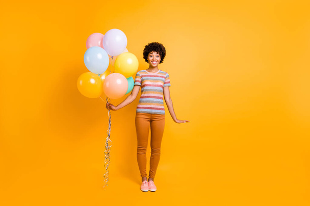 Full body photo of charming cheerful brunette curly hair dark skin teen girl hold many colorful baloons she got on anniversary holidays wear casual style outfit isolated over yellow color background - Foto, Imagem