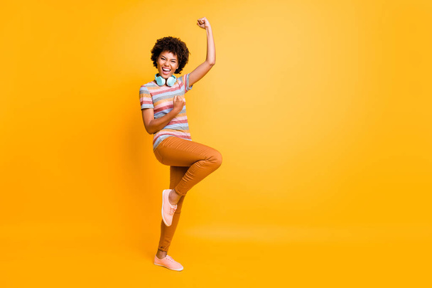 Full length body size photo of cheerful victorious excited crazy girl screaming yes wearing pants trousers footwear wireless headphones isolated over yellow vivid color background - Zdjęcie, obraz