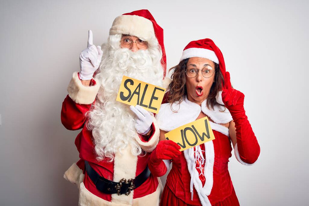 Pari yllään Santa puku tilalla wow ja myynti banneri yli eristetty valkoinen tausta osoittaa sormella ylös onnistunut idea. Poistunut ja onnellinen. Numero yksi.
. - Valokuva, kuva