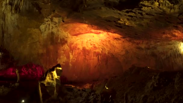 Интерьер пещеры или пещеры с тусклым освещением со сталактитами, свисающими с потолка, и сталагмитами, поднимающимися с пола
. - Кадры, видео