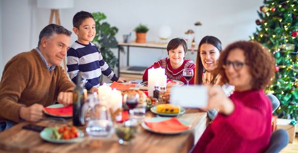 Όμορφη οικογένεια χαμογελά ευτυχισμένη και αυτοπεποίθηση. Τρώγοντας ψητό γαλοπούλα κάνει selfie από το smartphone γιορτάζει τα Χριστούγεννα στο σπίτι - Φωτογραφία, εικόνα