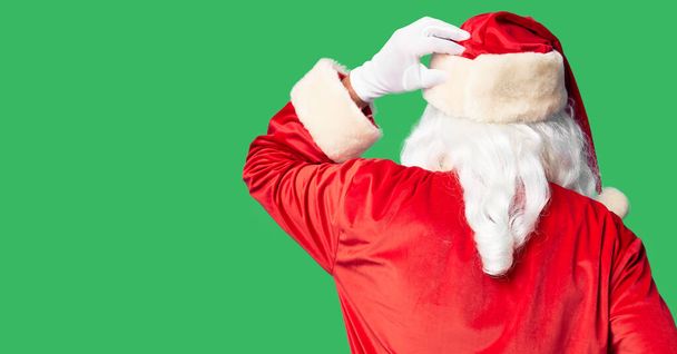 Homem bonito de meia idade vestindo traje de Papai Noel e barba de pé para trás pensando em dúvida com a mão na cabeça
 - Foto, Imagem