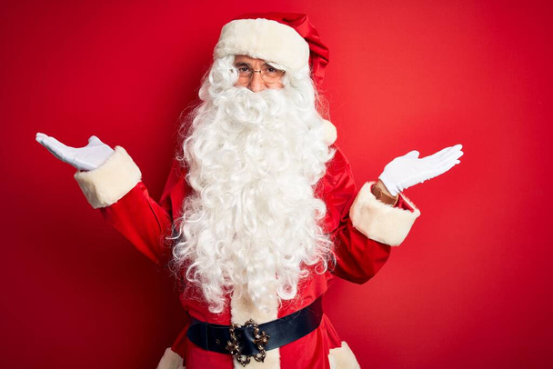 Medioevo bell'uomo che indossa il costume di Babbo Natale in piedi sopra isolato sfondo rosso sorridente mostrando entrambe le mani palme aperte, presentando e pubblicizzando confronto ed equilibrio
 - Foto, immagini