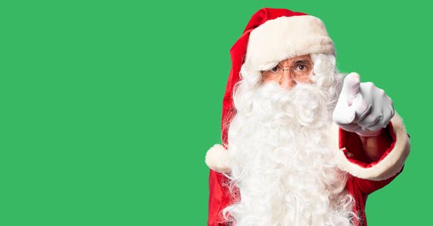 Pohledný muž středního věku v kostýmu Santa Clause a vousy stojící a ukazující nespokojeně a frustrovaně do kamery, naštvaný a rozzuřený na tebe - Fotografie, Obrázek