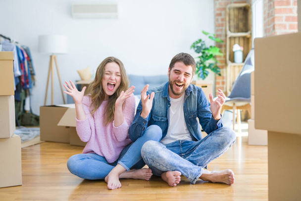 Fiatal gyönyörű pár költözik egy új házba, a padlón ülve őrülten és őrülten ünneplik a sikert, felemelt karokkal és izgatottan sikoltozó csukott szemmel. Nyertes koncepció - Fotó, kép