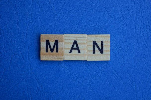 Palavra homem feito de letras de madeira marrom encontra-se em uma mesa azul
 - Foto, Imagem