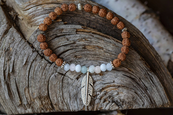 Bracelet yoga en pierre minérale avec pendentif en plumes métalliques sur fond bois
 - Photo, image