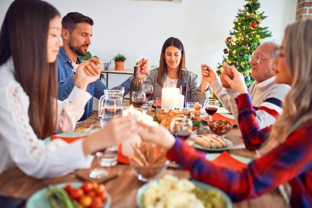 Mooie familie bijeenkomst glimlachend gelukkig en vol vertrouwen. Bidden het nemen van handen voor het eten van geroosterde kalkoen vieren Kerstmis thuis - Foto, afbeelding