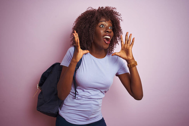 Jeune femme afro-touristique africaine portant un sac à dos debout sur fond rose isolé fou et fou criant et criant avec une expression agressive et les bras levés. Concept de frustration
. - Photo, image