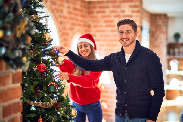 Evdeki Noel ağacının yanında mutlu ve kendinden emin gülümseyen genç çift. - Fotoğraf, Görsel