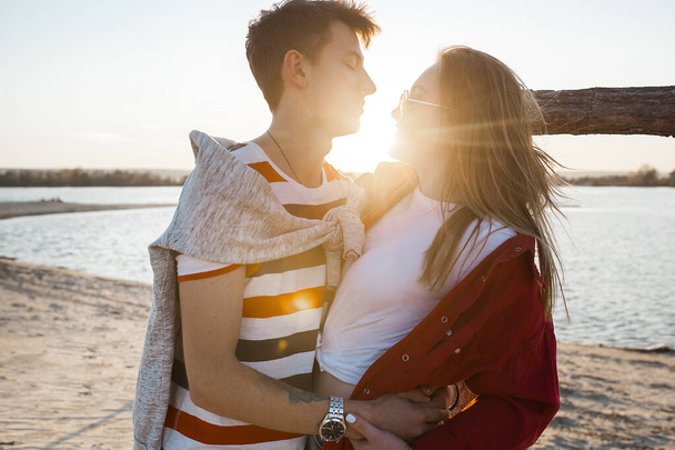 Liebendes junges Paar beim Sonnenuntergang am Strand. Liebe. Mann und Frau küssen und umarmen sich auf sommerlichem Hintergrund. - Foto, Bild