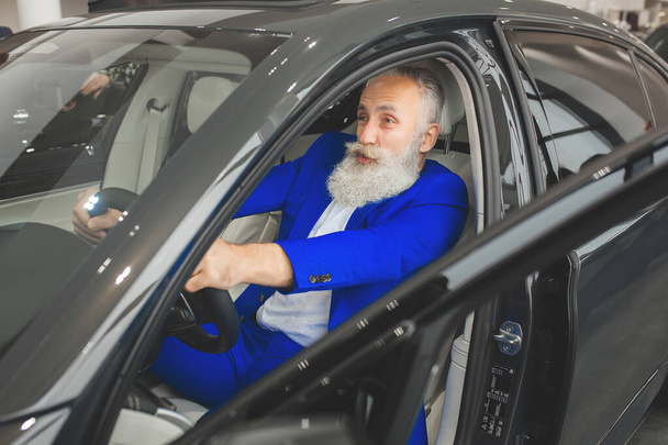 Oude stijlvolle man in de luxe auto. Man met baard en mosterd rijdende auto. autoverkoop salon. - Foto, afbeelding