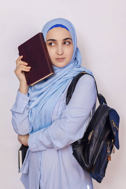 Moderni muslimioppilas hijabissa. Nuori Lähi-idän opiskelija, jolla on reppu ja muistilehtiöitä. Eristetty valkoisella taustalla. Muotokuva nuorten arabialainen nainen opiskelija
 - Valokuva, kuva