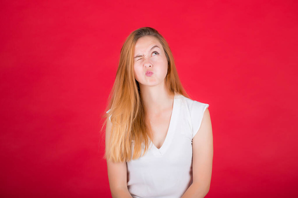 Young woman grimaces at the camera. Girl in a white shirt on a red background. - Fotó, kép