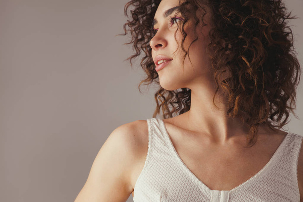 Beautiful woman with curly hair against gray background - Fotoğraf, Görsel