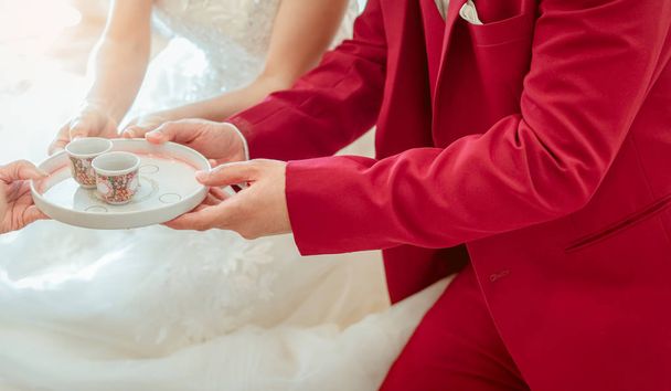 Γαμπρός και νύφη σε τελετή τσαγιού την ημέρα της τελετής του γάμου. Νύφη και γαμπρός σε λευκό νυφικό και κόκκινο κοστούμι καθίσει anf άρση φλιτζάνι τσάι. Γάμος ή γάμο. Ξεκινήστε τη ζωή του ζευγαριού. Κινεζική κουλτούρα γάμου. - Φωτογραφία, εικόνα