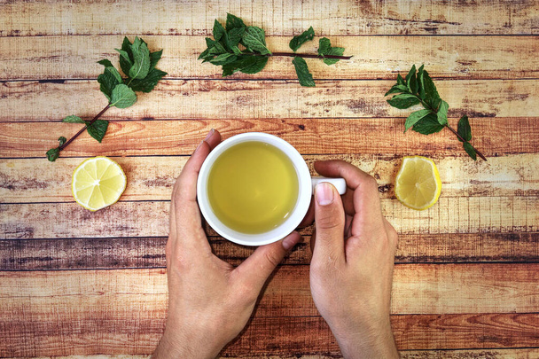 Drankjes warme salvia thee voor gezond te houden in de winter dagen. Natuurlijke en zelfgemaakte kruidenthee als muntblad, citroen of salvia thee. Jonge zieke man drinken hete thee en warmt handen over kopje thee - Foto, afbeelding