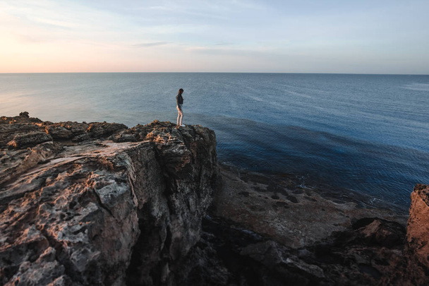 Woman traveler standing near sea on top of cliff in summer mountains and enjoying view of sea and nature. Cape Greco, Cyprus, Mediterranean Sea. Sunrise - Photo, Image