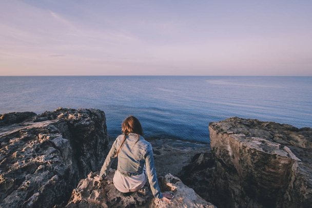 Mulher viajante sentado perto do mar no topo do penhasco em montanhas de verão e desfrutando de vista do mar e da natureza. Cabo Greco, Chipre, Mar Mediterrâneo. Nascer do sol
 - Foto, Imagem
