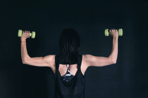 Athletic woman doing exercise for arms. Working out with dumbbells on black background - Fotoğraf, Görsel