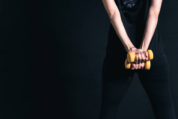 Back view of woman hands holding two yellow dumbbells on her back - Fotoğraf, Görsel