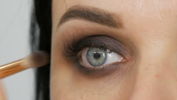 Professionele oogmake-up. Stylist make-up kunstenaar past make-up op jonge vrouw met een speciale borstel in een schoonheidssalon - Video